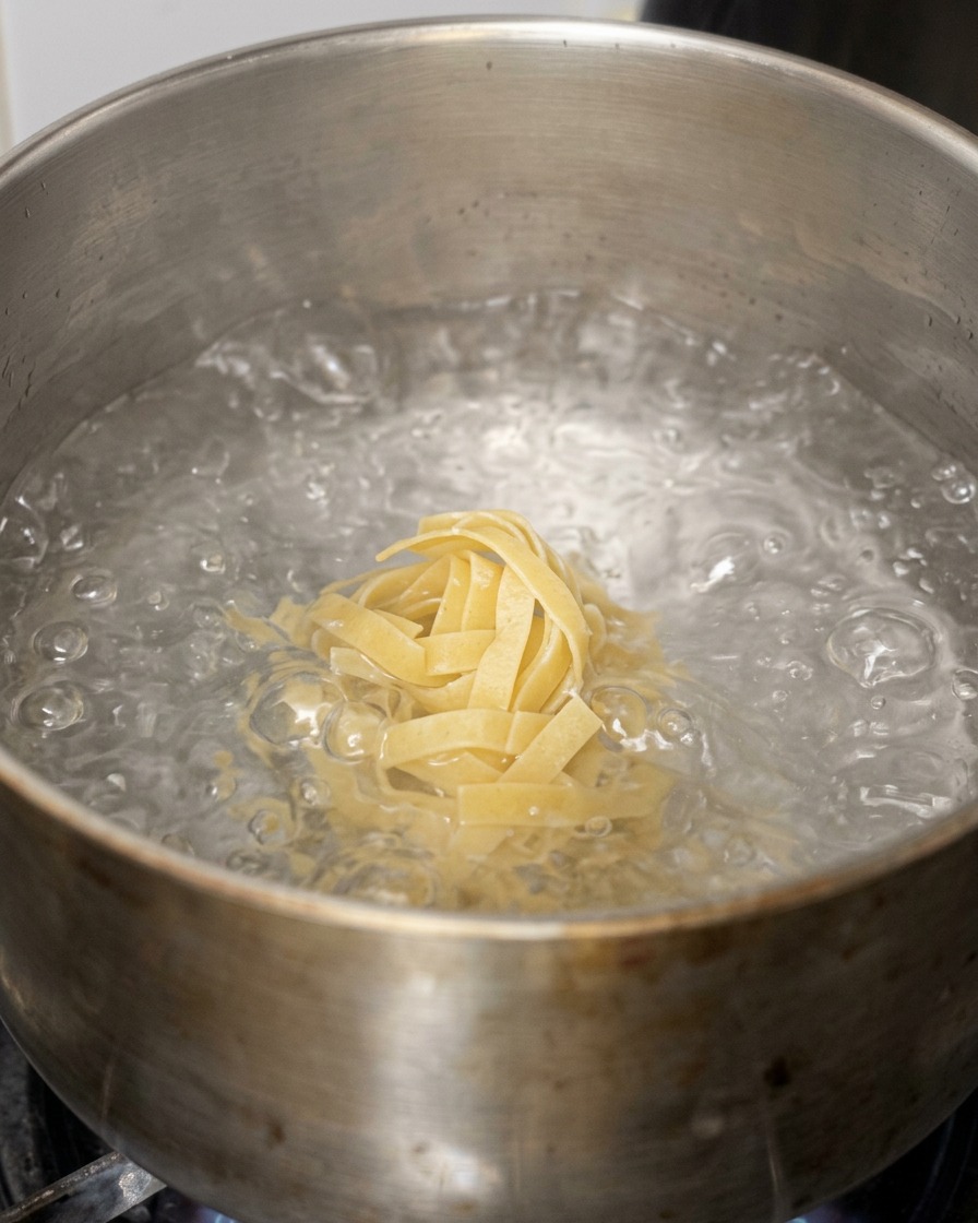 沸騰した鍋のお湯に、平打ちの幅広パスタを入れている様子。
