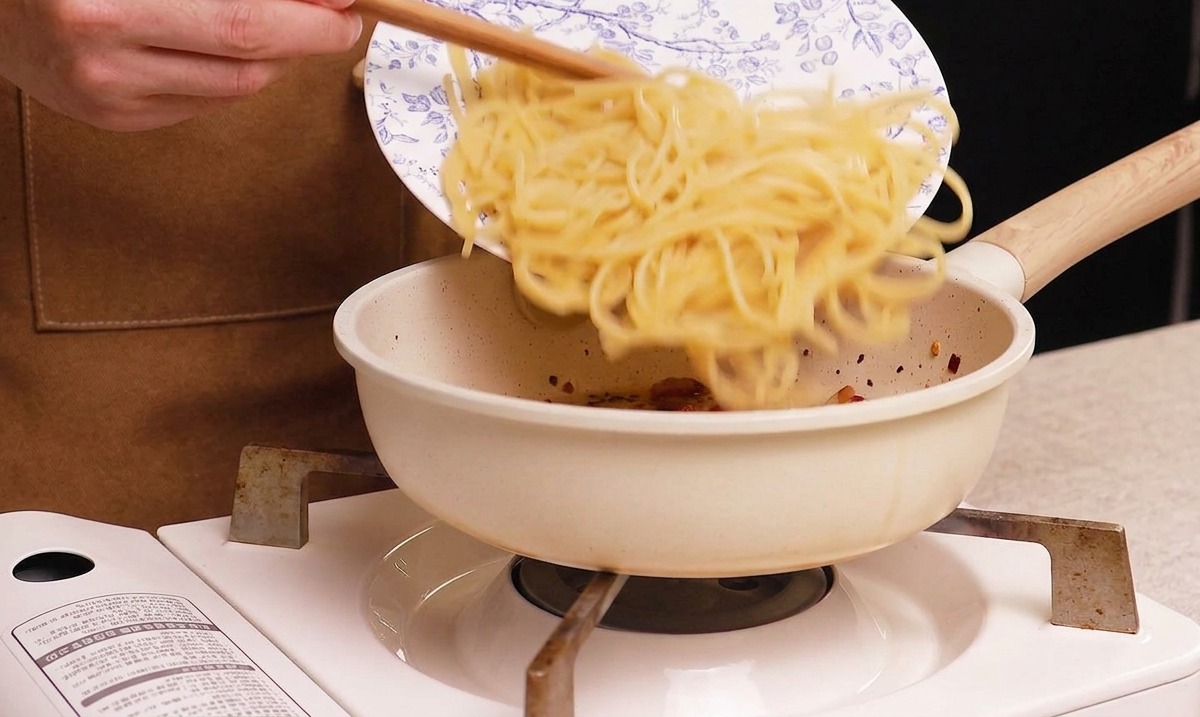 茹で上がったスパゲッティをグアンチャーレの入ったフライパンに移している様子。
