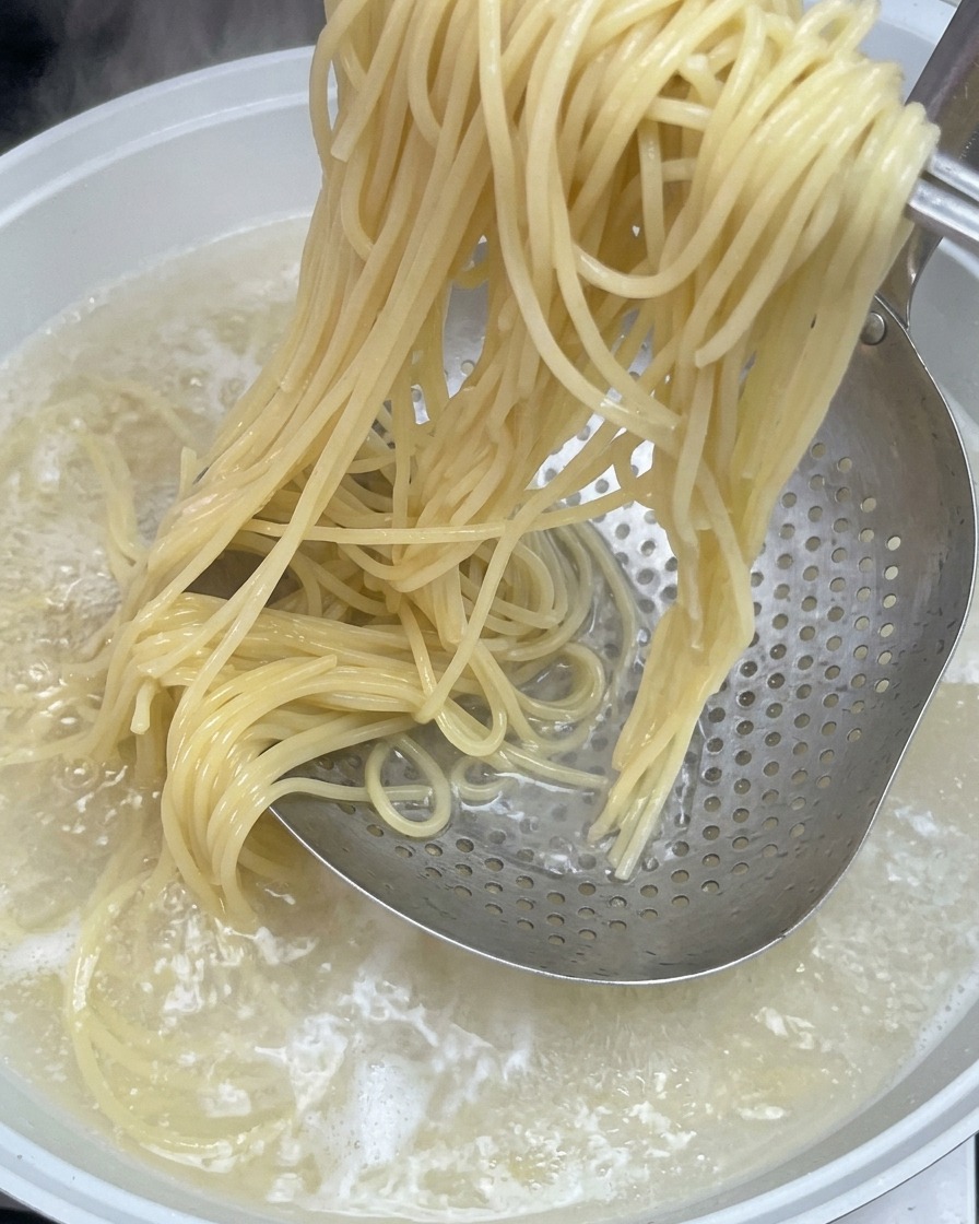 茹で上がったスパゲッティを金属製のストレーナーですくい上げる様子。