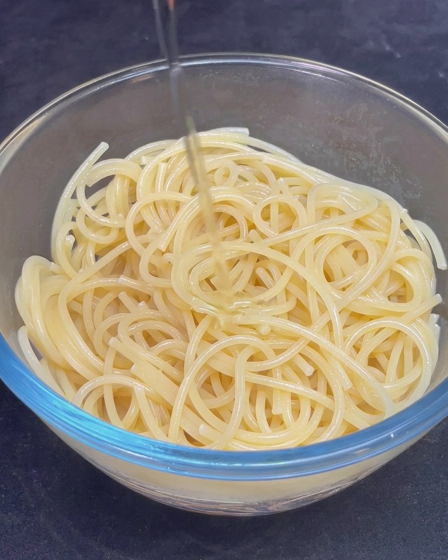 ボウルに入ったスパゲッティに黄金色のオリーブオイルを回しかける様子。