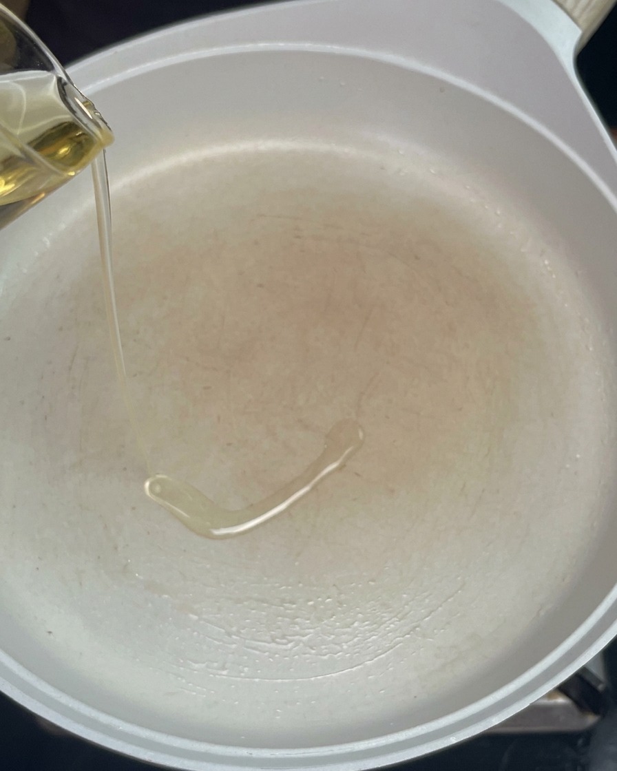 予熱した白いフライパンにサラダ油を注ぐ様子。