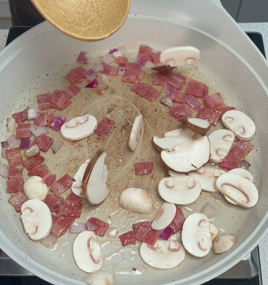 スライスしたマッシュルームとしいたけをフライパンに加え、木べらで混ぜる様子。