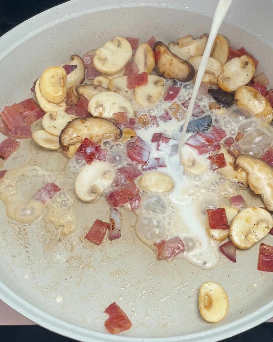 具材が入ったフライパンに白い牛乳を注ぎ入れる様子。