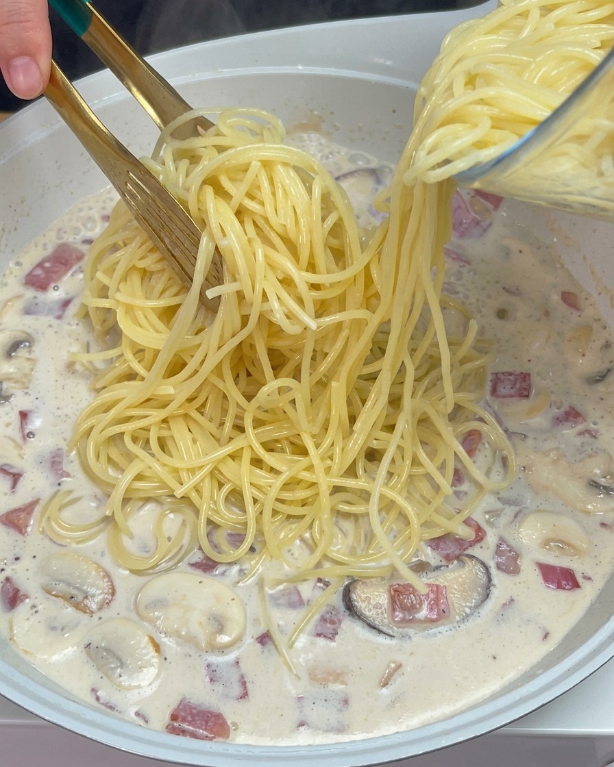 沸騰したクリームソースに、茹でておいたスパゲッティを加える様子。