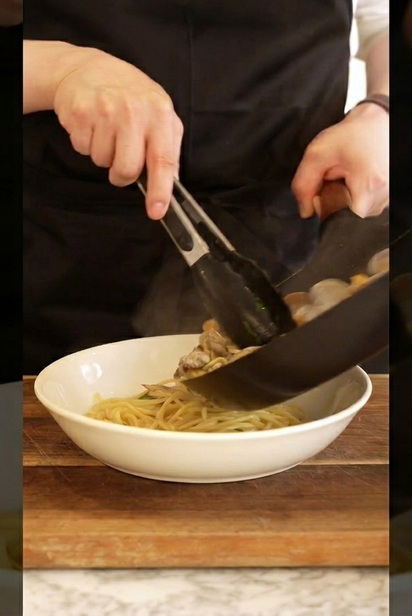 トングを使ってパスタをボウルに盛り付けている様子。