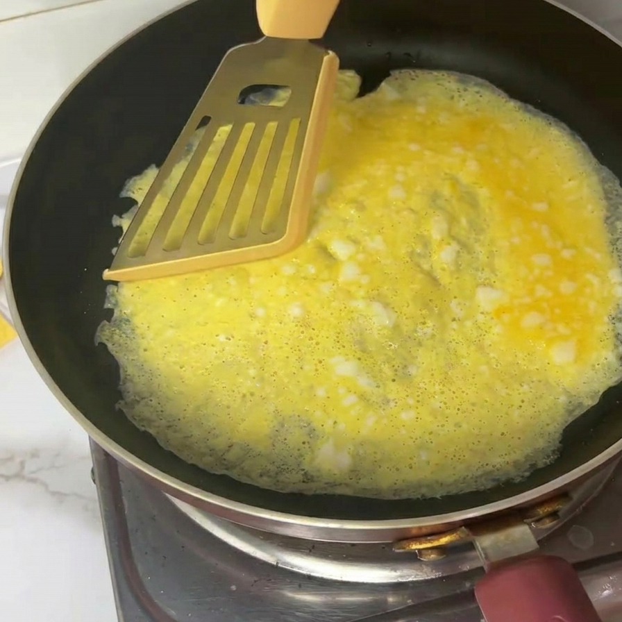 フライパンの上で、スパチュラを使って薄焼き卵を4等分にカットする様子。