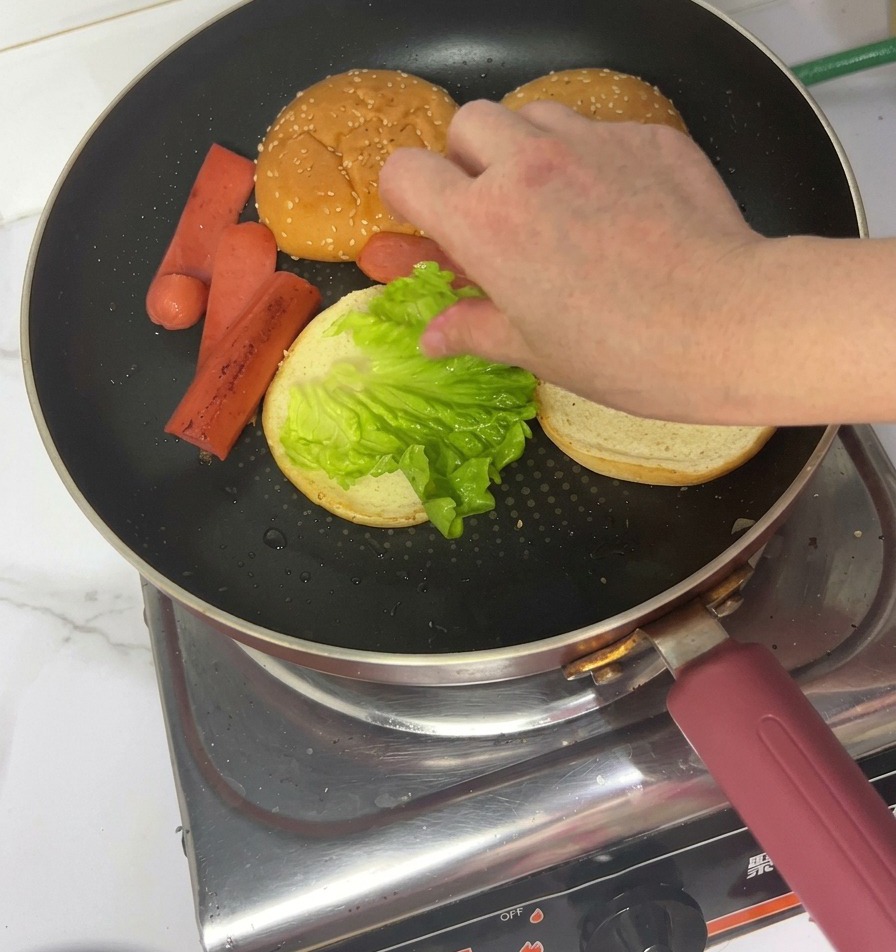 焼いたバンズの上に、新鮮なレタスをのせる様子。