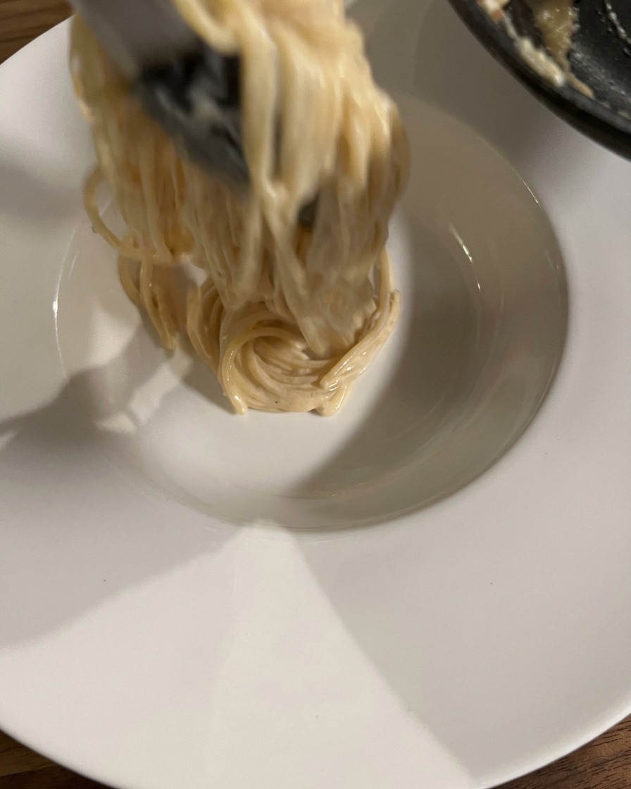 トングでパスタを高く巻き上げ、お皿の中央に盛り付けている様子。