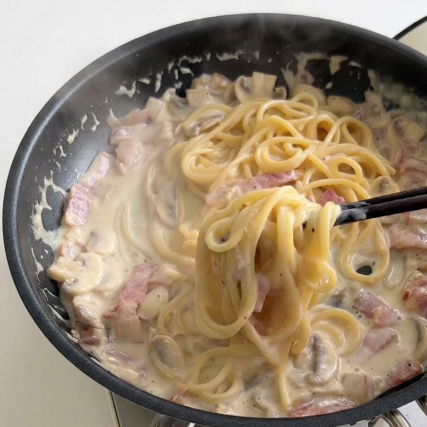 フライパンの中でパスタをトングで回し、ソースを煮詰める様子。