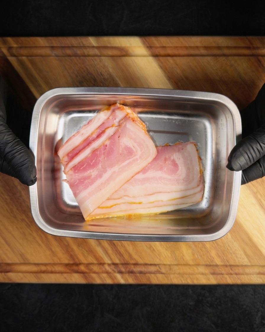 長方形のトレイに並べられた調理前のベーコンスライス。