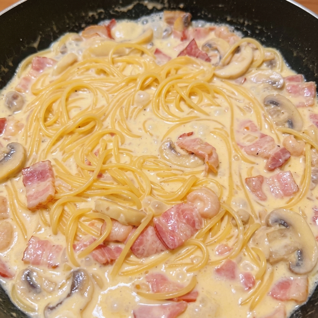 濃厚なソースが入ったフライパンでスパゲッティをトングを使って和えている様子。