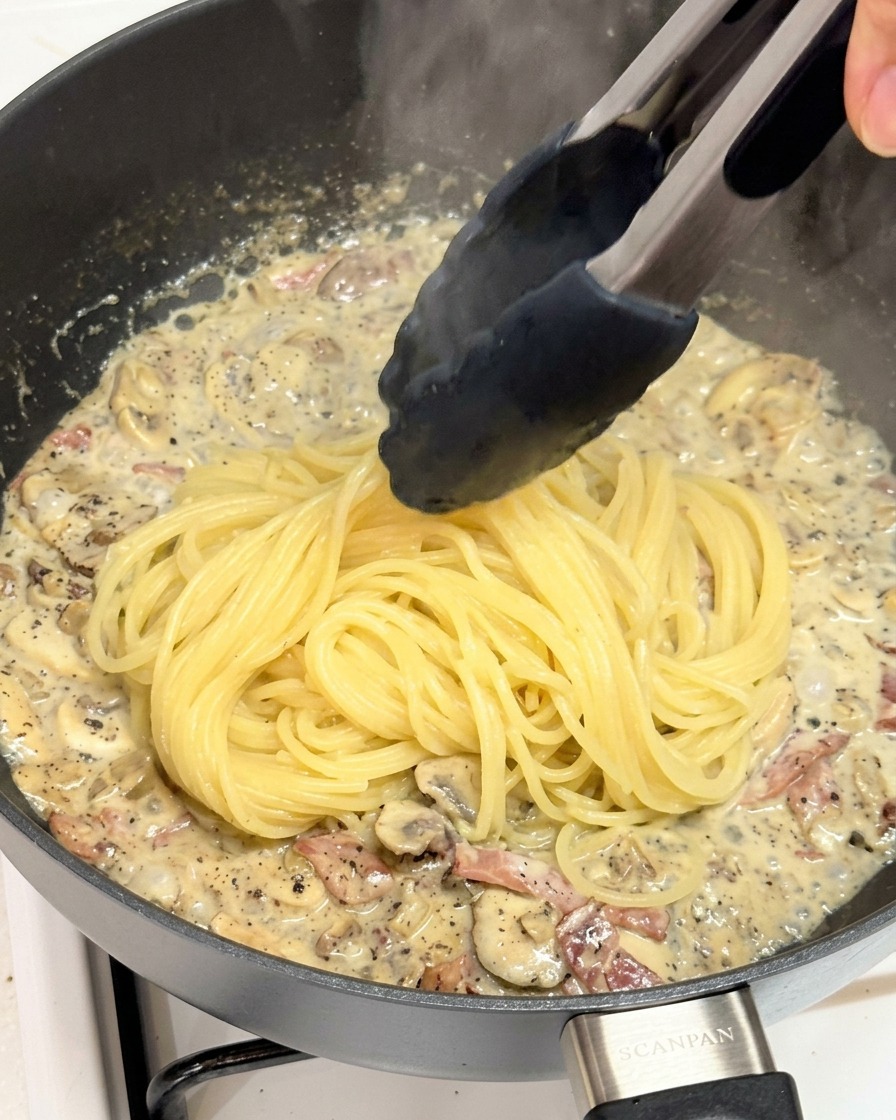 茹で上がったパスタをソースの入ったフライパンに移す様子。