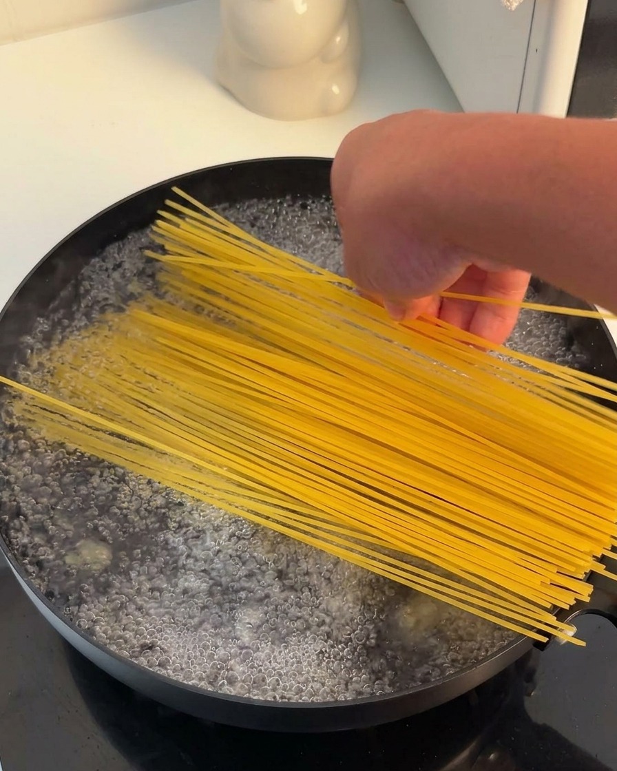 沸騰したお湯が入った黒い鍋に、乾燥したスパゲッティの束を入れている様子。