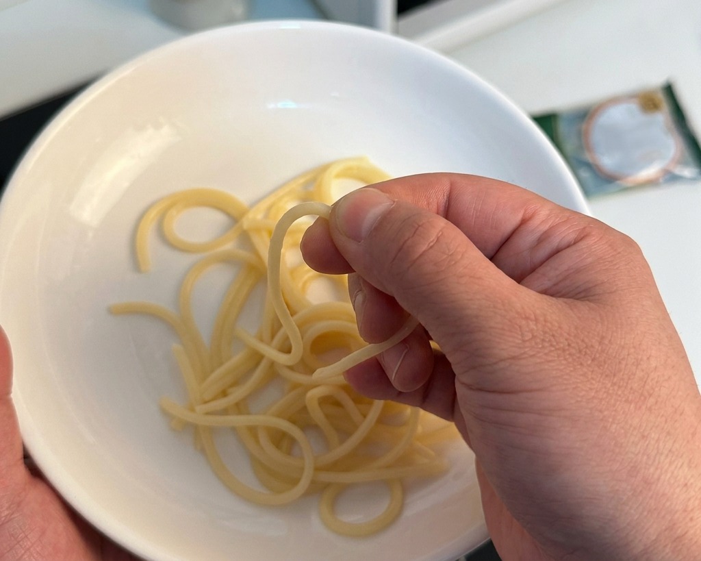 白いボウルの上でスパゲッティを一本つまみ、硬さを確認している様子。