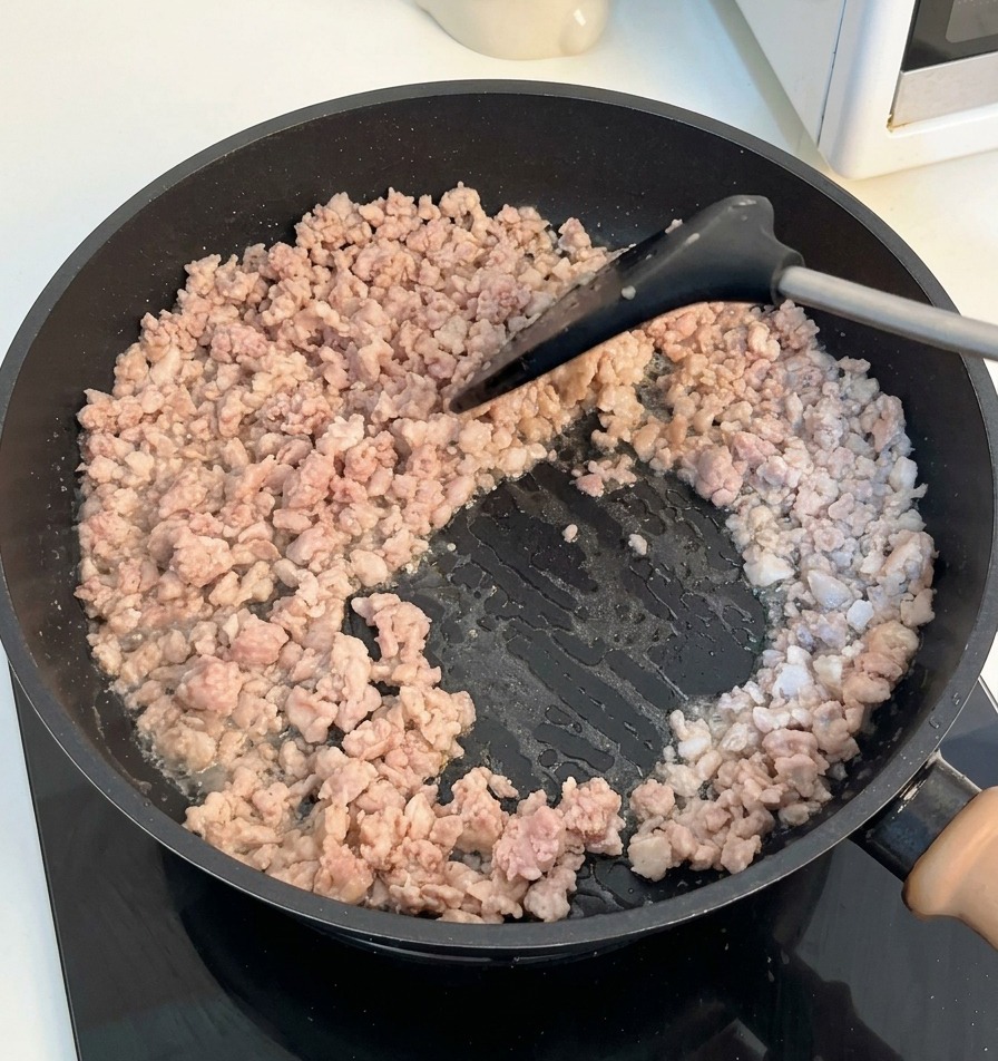 黒いヘラを使って、フライパンの中の挽肉をほぐしながら炒めている様子。