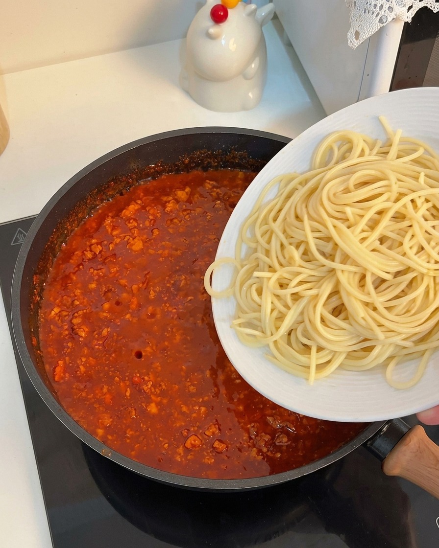 濃厚なミートソースが入ったフライパンに、茹で上がったスパゲッティを入れている様子。