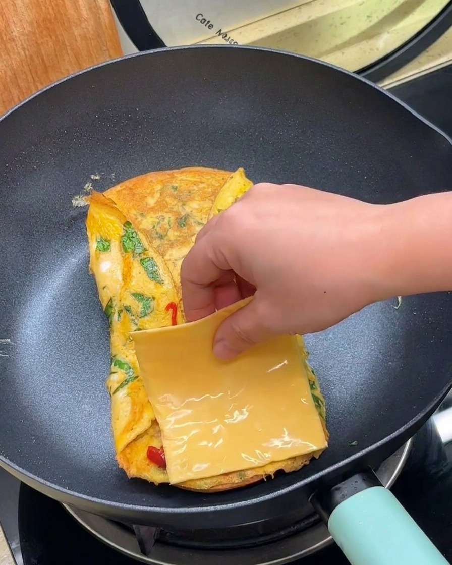 フライパンの中の卵の上にスライスチーズをのせている様子。