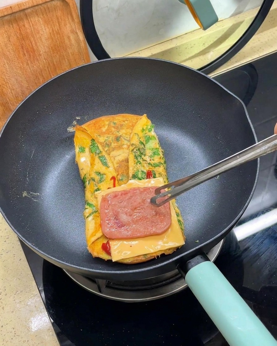 トングを使って、チーズの上に焼いたベーコンをのせている様子。
