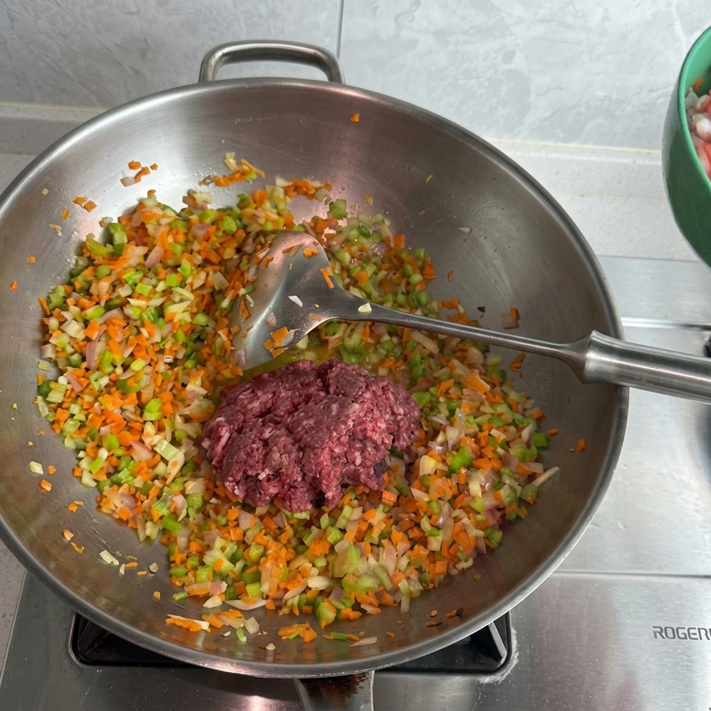 ステンレスのウォックに入った野菜の上に、生の豚ひき肉と牛ひき肉が乗っている様子。