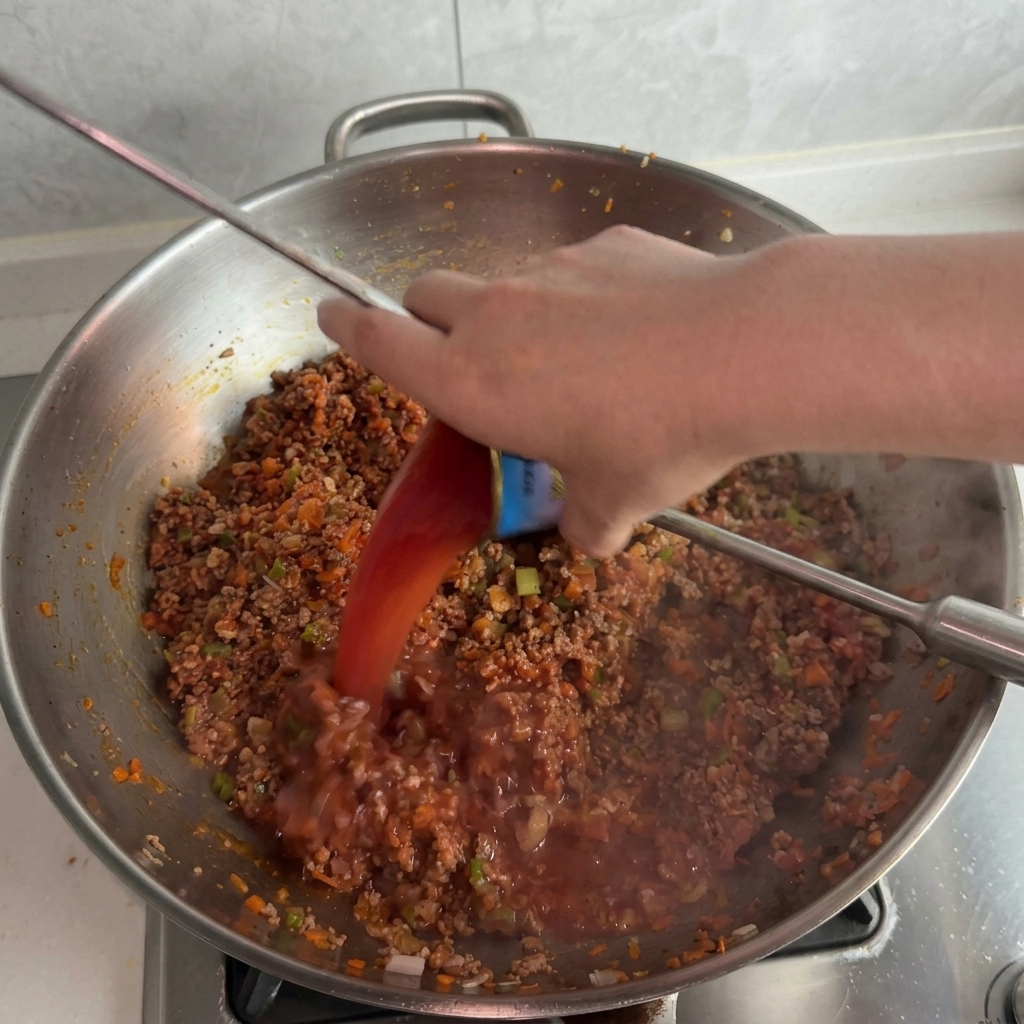 トマトペーストの空き缶を使って、肉ソースの入ったウォックに水を入れる様子。