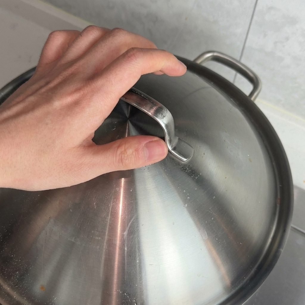 鍋に金属製の蓋を被せる手。