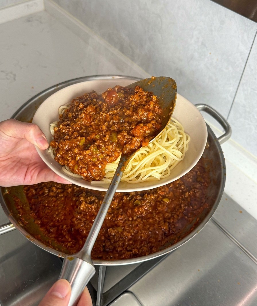 茹でたてのスパゲッティに、たっぷりのミートソースを盛り付けている様子。