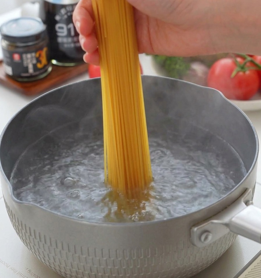 沸騰したお湯が入ったグレーの鍋に、乾燥スパゲッティを垂直に入れる様子。