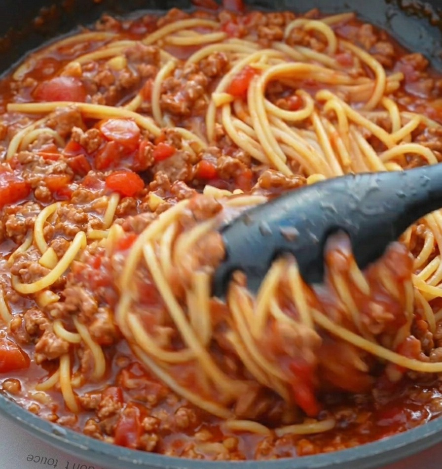 フライパンの中で、トングを使って茹でたパスタをソースと和えている様子。