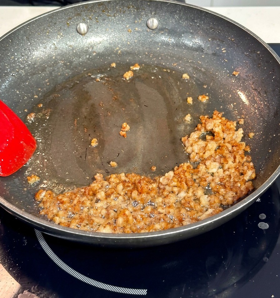 フライパンの中で、赤色のヘラを使って豚ひき肉を炒め、焼き色をつけている様子。