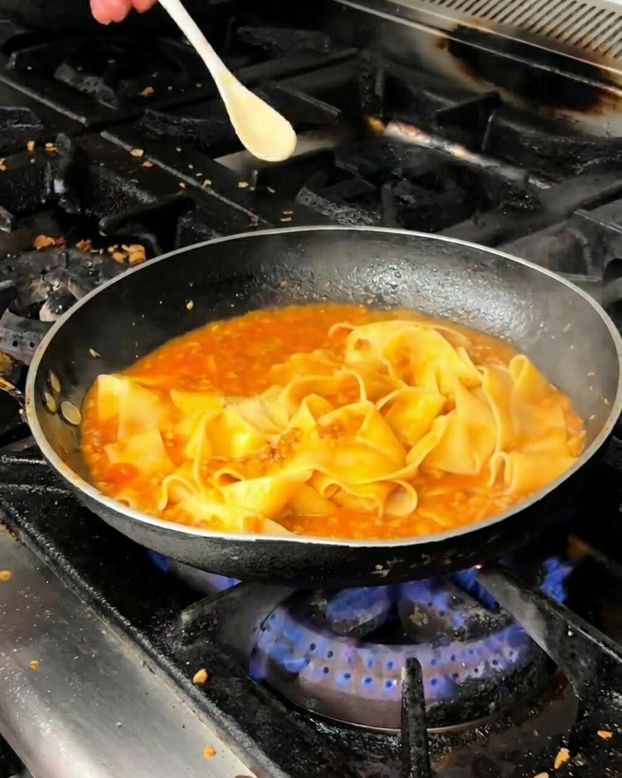 ソースの中でパスタを和えながら調味料を振りかける様子