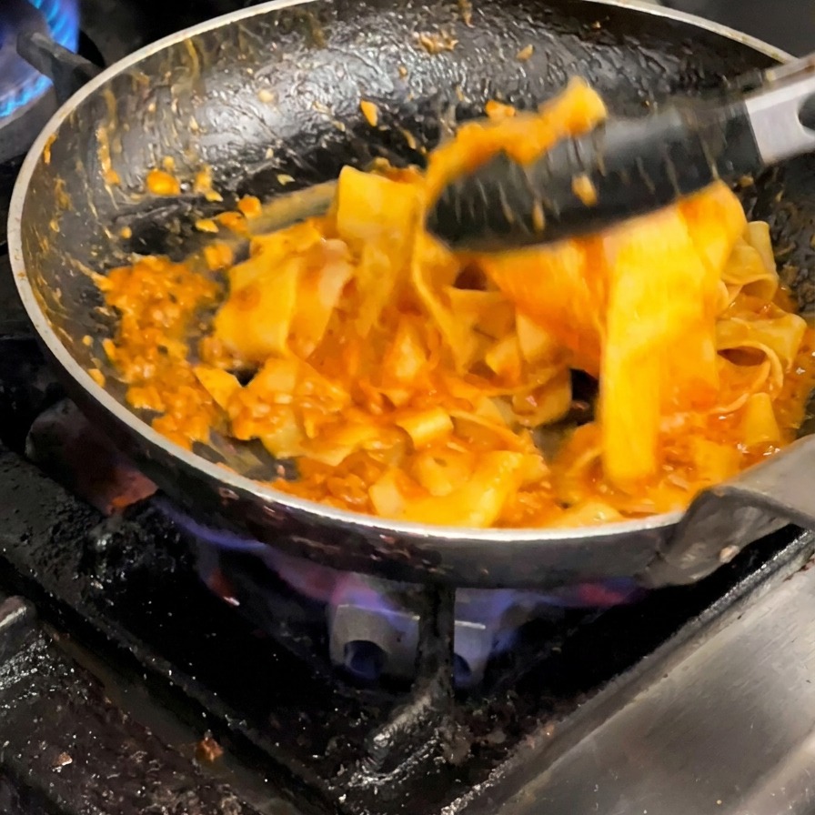 トングを使ってパスタとミートソースを豪快に混ぜ合わせる様子