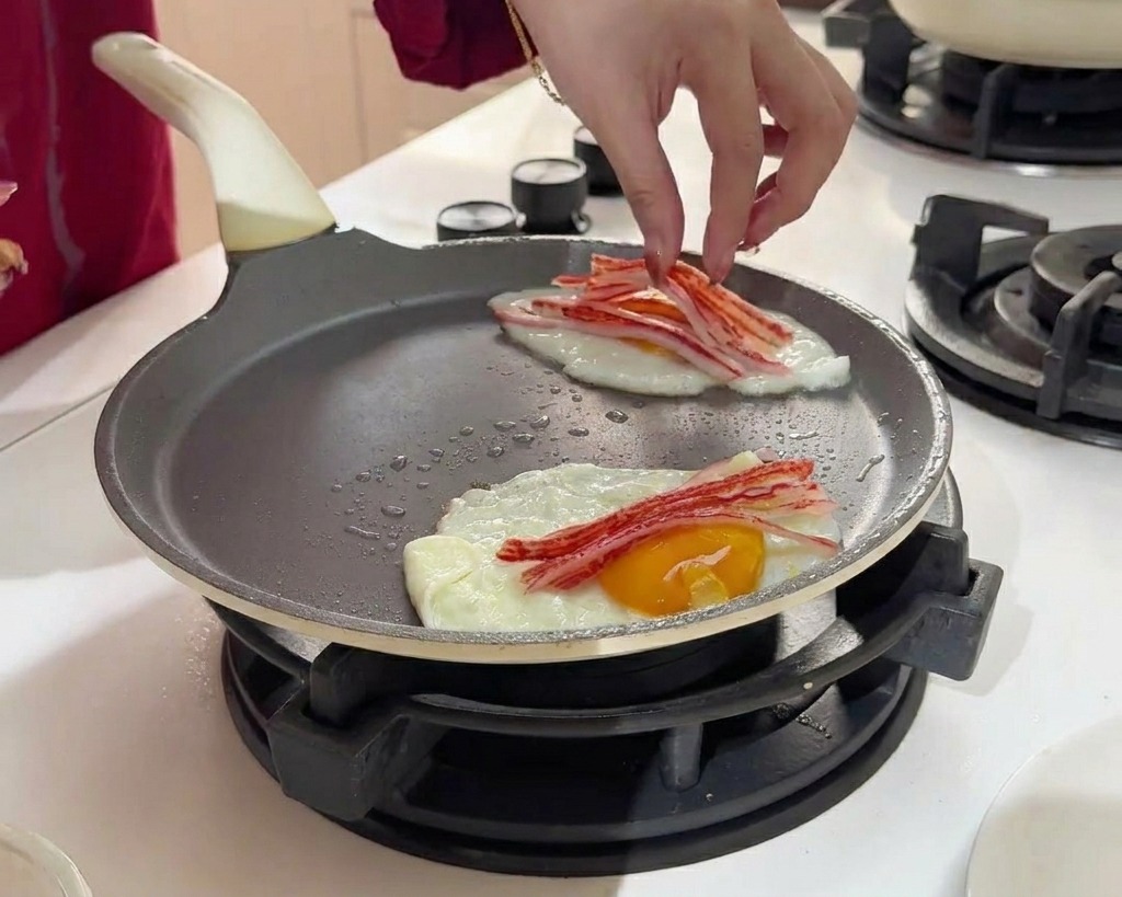 焼いている卵の上に、細く裂いたカニカマをのせている様子。