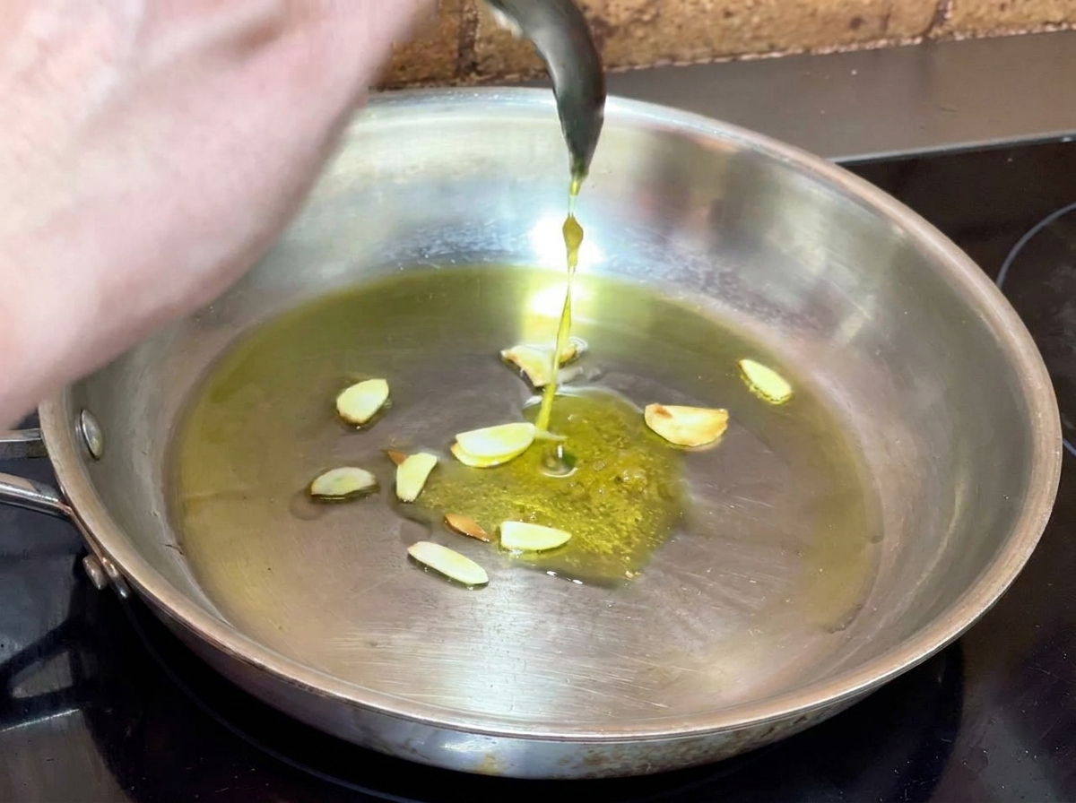 スライスにんにくの入ったフライパンに、準備しておいたにんにくペーストをスプーンで加えている様子。