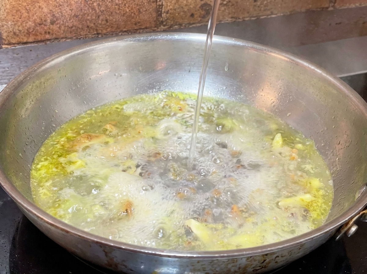 にんにくオイルが沸いているフライパンに、お玉でパスタのゆで汁を注いでいる様子。