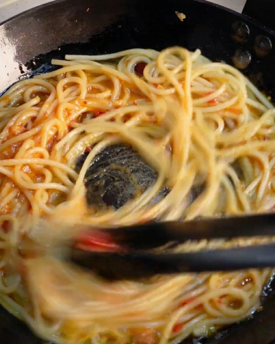 フライパンの中でトングを使ってスパゲッティを勢いよく混ぜ合わせている様子。