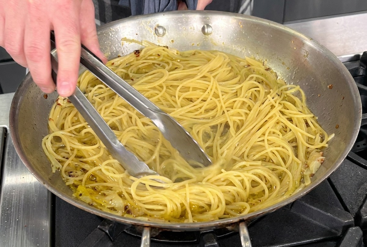 フライパンの中でパスタとオイルソースをトングで手早く混ぜ合わせる様子