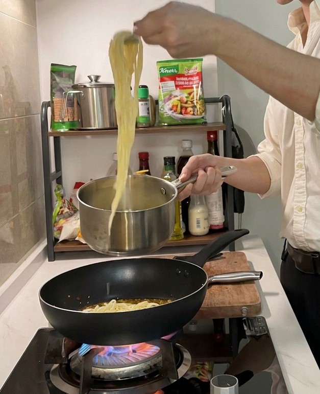 トングを使って茹で上がったパスタをフライパンに移す様子。