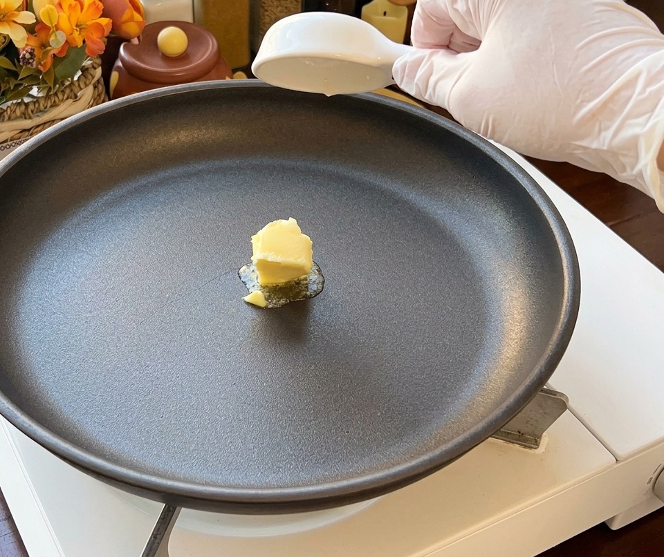 黒いノンスティックフライパンの中央で溶け始める黄色いバター。