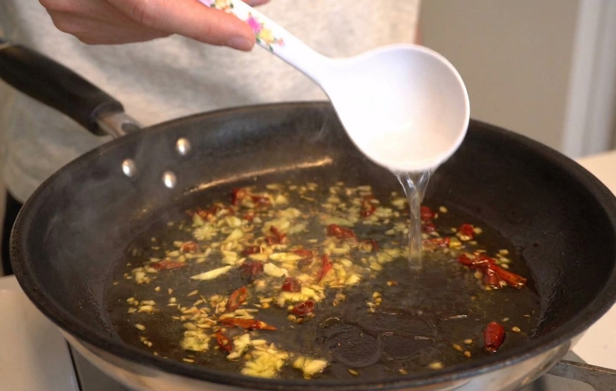 にんにく、オイル、唐辛子が熱されたフライパンに、白いお玉でパスタのゆで汁を注いでいる様子。
