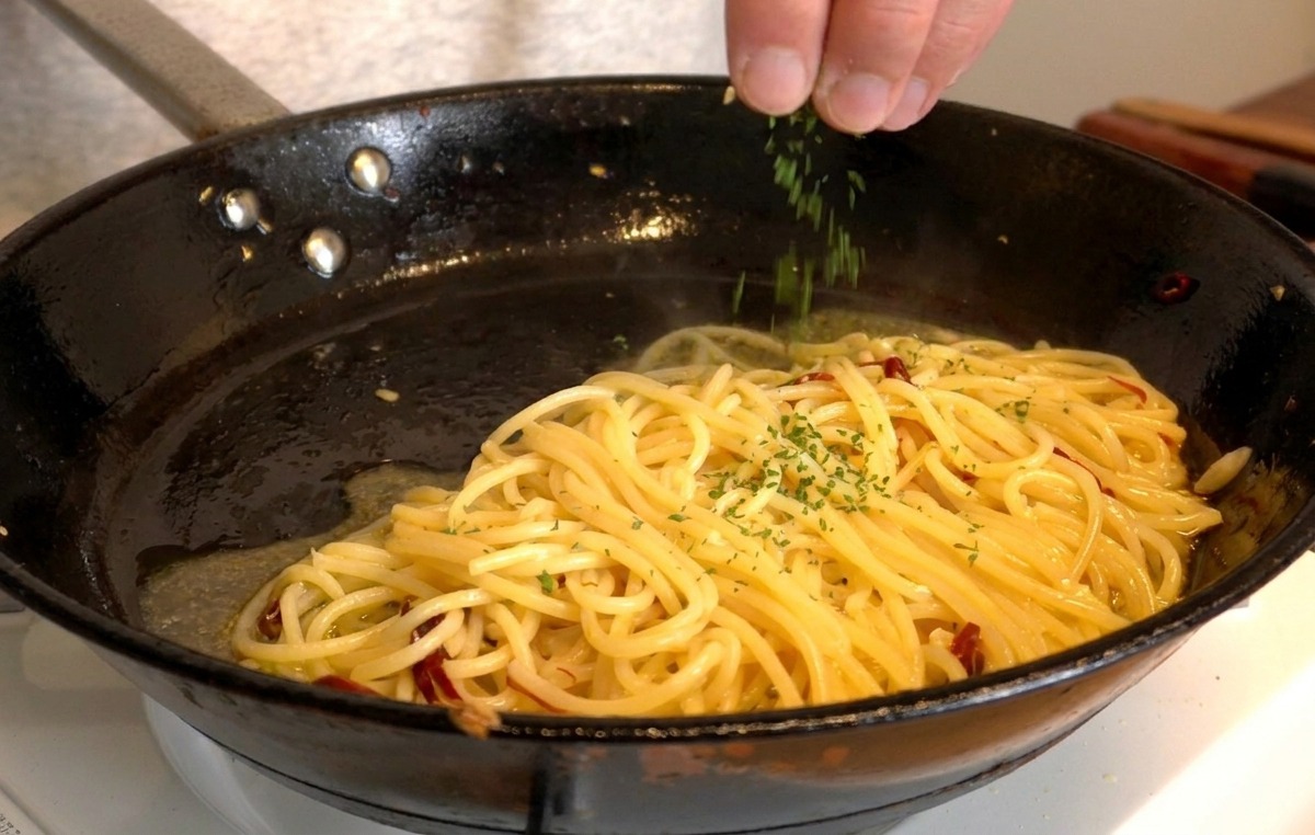 ツヤツヤに仕上がったスパゲッティの上に、細かく刻んだ緑のフレッシュパセリを手で散らしている様子。