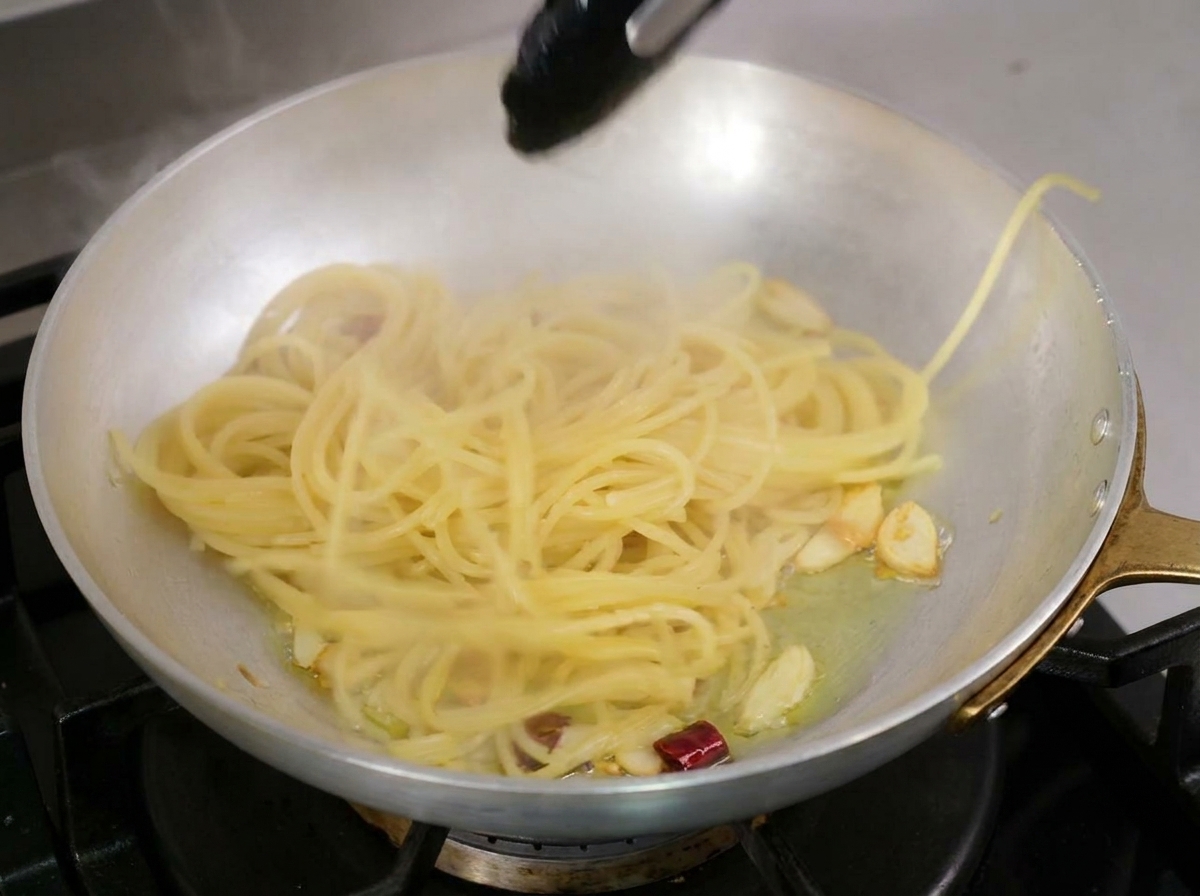 トングを使って、茹で上がったスパゲッティをオイルの入ったフライパンに移している様子。