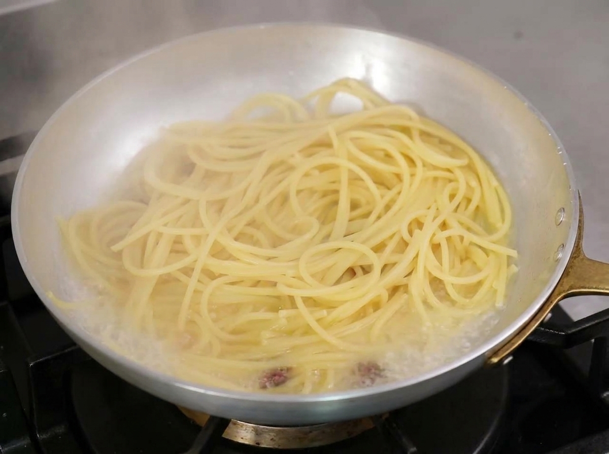 スパゲッティが入ったフライパンに、お玉で茹で汁を加えている様子。