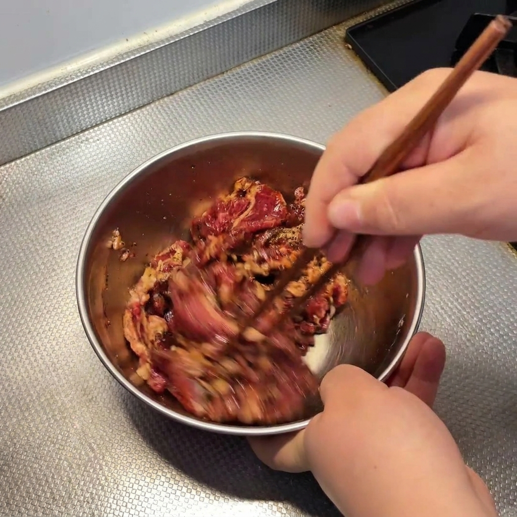 ボウルの中で牛肉と調味料を菜箸で手早く混ぜ合わせている様子。