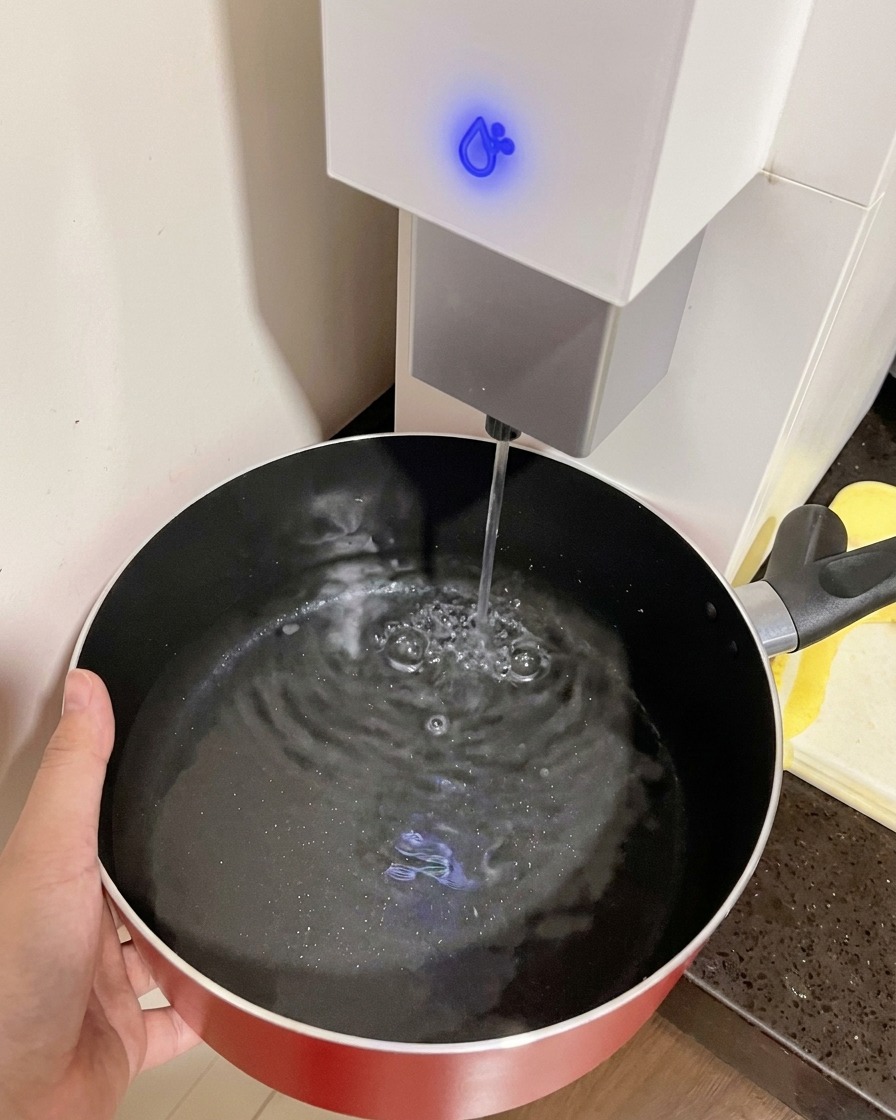 ウォーターサーバーから赤い鍋に水を入れている様子。