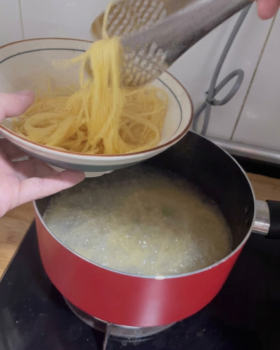 トングを使って茹であがったスパゲッティをボウルに移している様子。