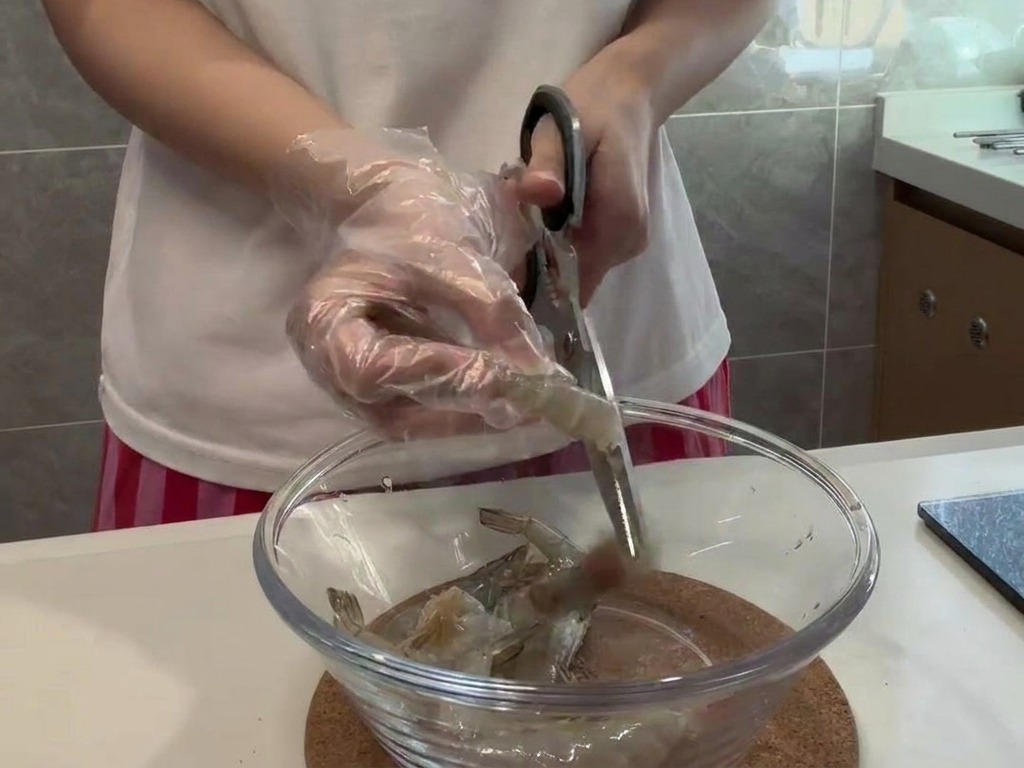調理用手袋をして、ハサミでエビの背中を丁寧に処理している様子。