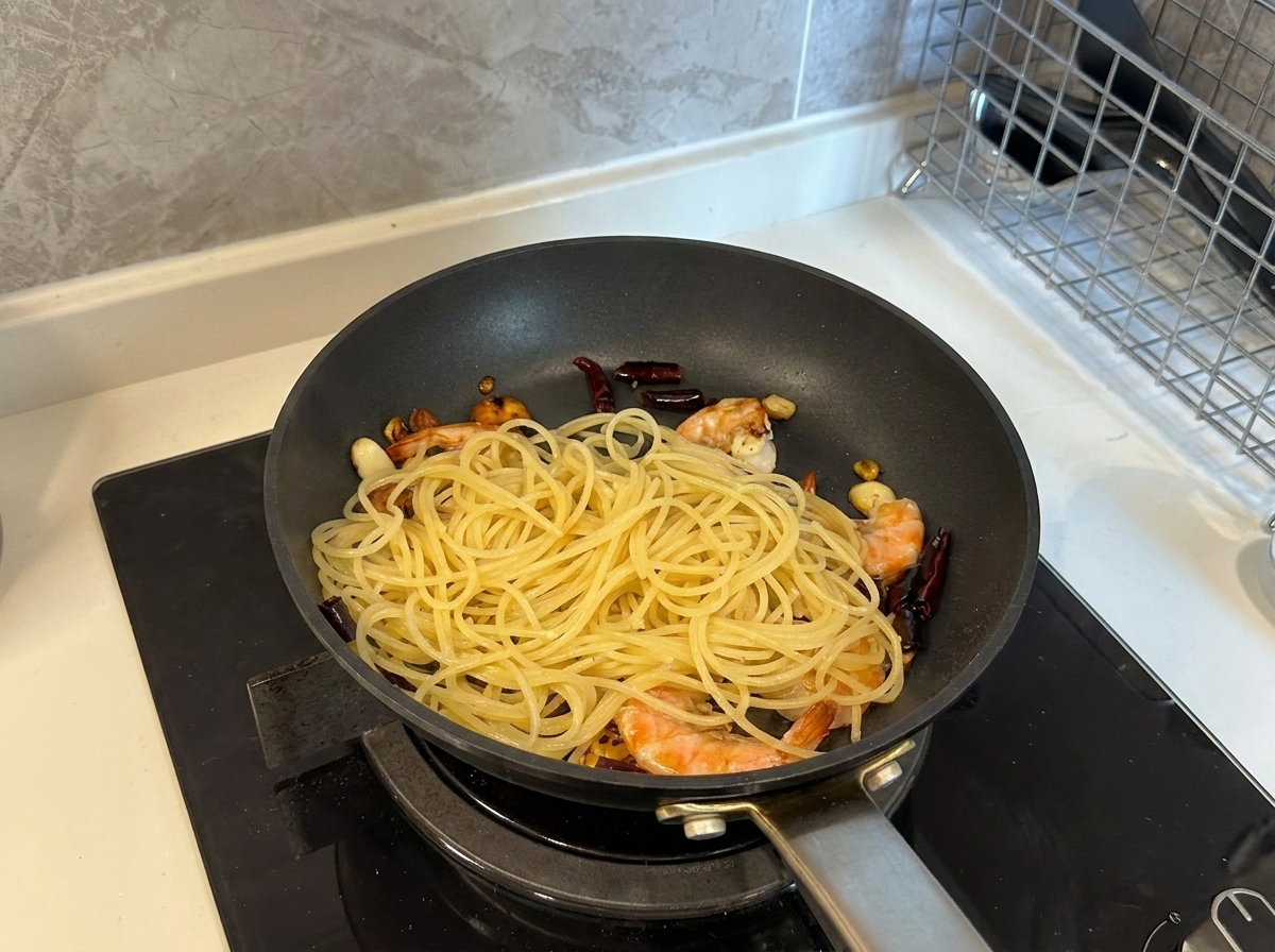 エビとニンニクが入ったフライパンに、茹でたてのスパゲッティを加えている様子。
