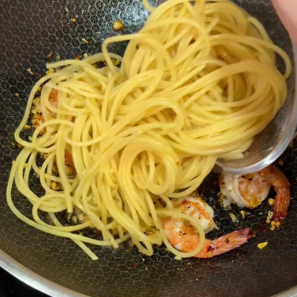 海老とにんにくが入ったフライパンに、茹で上がったスパゲッティを加えている様子。