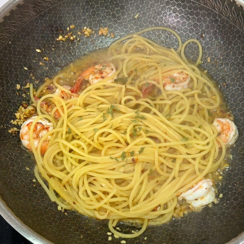 フライパンの中のパスタに、鮮やかな緑色の刻みパセリを散らしている様子。