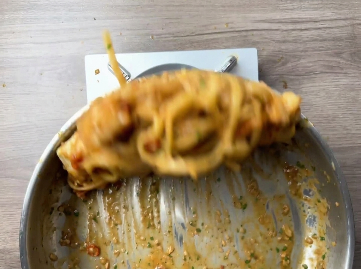 フライパンでパスタと海老を勢いよく混ぜている様子。